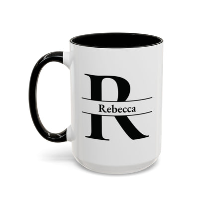 An accent color 15oz ceramic mug with a black interior, black handle, and a black graphic of a stylized letter R with a banner reading 'Rebecca' on the front. Left handle view.