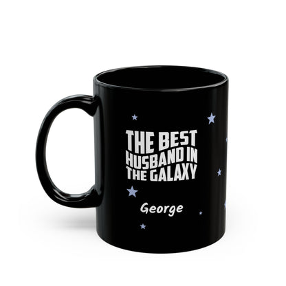 Black 11oz mug with small light blue stars and white text 'Best Husband in the Galaxy' with a personalize name below. Left handle view. Mug is placed on a white background
