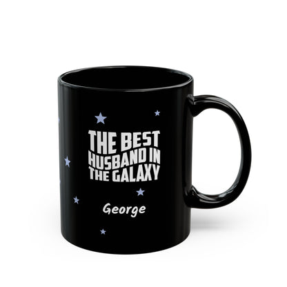 Black 11oz mug with small light blue stars and white text 'Best Husband in the Galaxy' with a personalize name below. Right handle view. Mug is placed on a white background