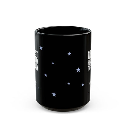 Side view of black ceramic 15oz mug with a starry night sky design, featuring white text on the sides and small light blue stars scattered across the surface. Mug is shown against a plain white background.