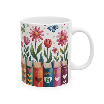 A white ceramic 11oz mug decorated with a colorful illustration of flowers, butterflies, and book spines on a white background. A personalized initial in a heart, on a book spine. Right handle view.