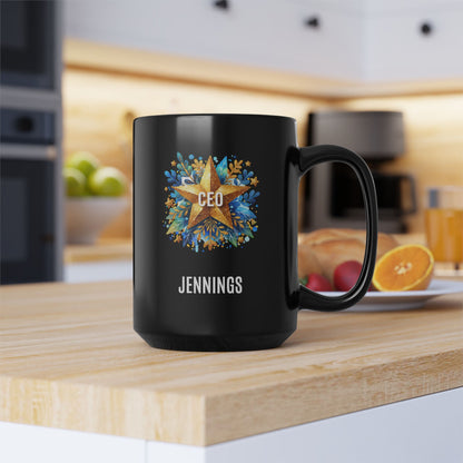 A glossy black 15oz ceramic mug with a custom printed design featuring a gold star, blue floral accents, the text 'CEO' in the center, and personalized name 'JENNINGS' printed below in white. sitting on a wooden countertop in a blurred kitchen setting.