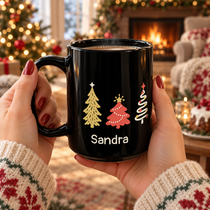A person holds a black ceramic 15oz mug with a holiday design in a cozy living room setting. The mug features seven colorful Christmas trees around the mug, and the name 'Sandra' in warm white text.