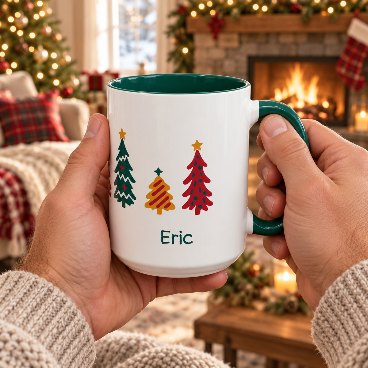 A person holds a white ceramic 15oz mug with a dark green interior and handle, decorated with seven colorful Christmas trees around the mug and the name 'Eric' printed below. The background shows a cozy living room with a lit fireplace, stockings, and a Christmas tree.