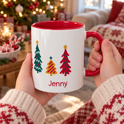 A girl holds a white ceramic 11oz mug with a red interior and red handle, decorated with seven colorful Christmas trees  around the mug and the name 'Jenny' in red. The background shows a cozy, blurred living room with a decorated Christmas tree and holiday decorations.