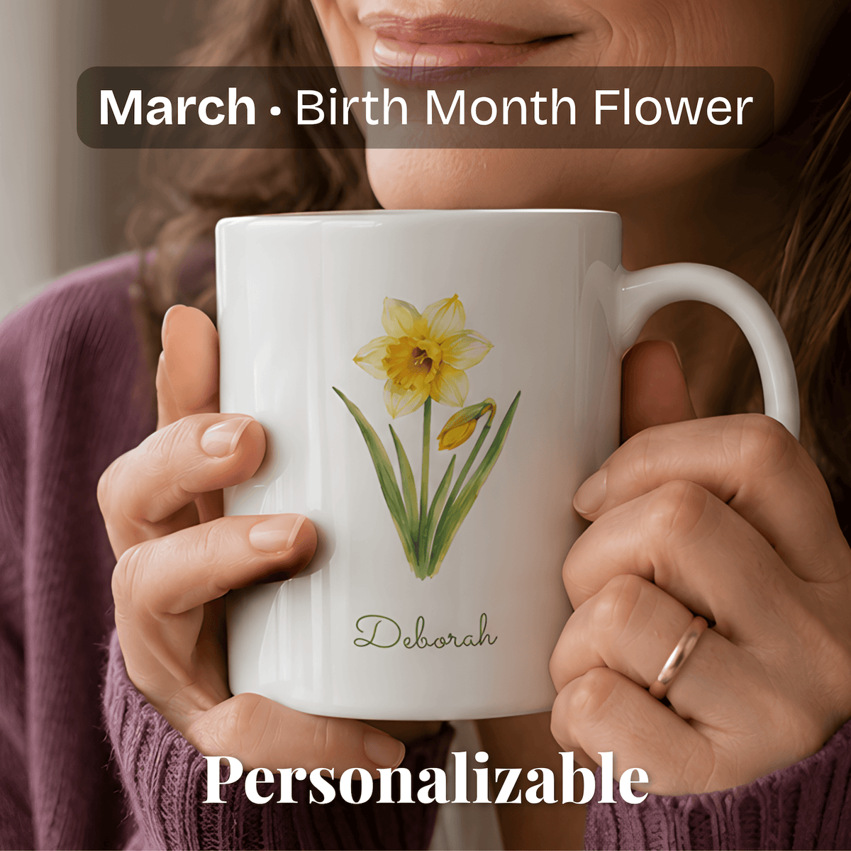A woman holds a white ceramic mug with daffodil birth flower and personalized name at bottom.
