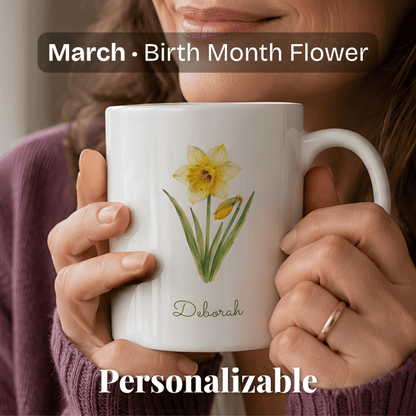 A woman holds a white ceramic mug with daffodil birth flower and personalized name at bottom.
