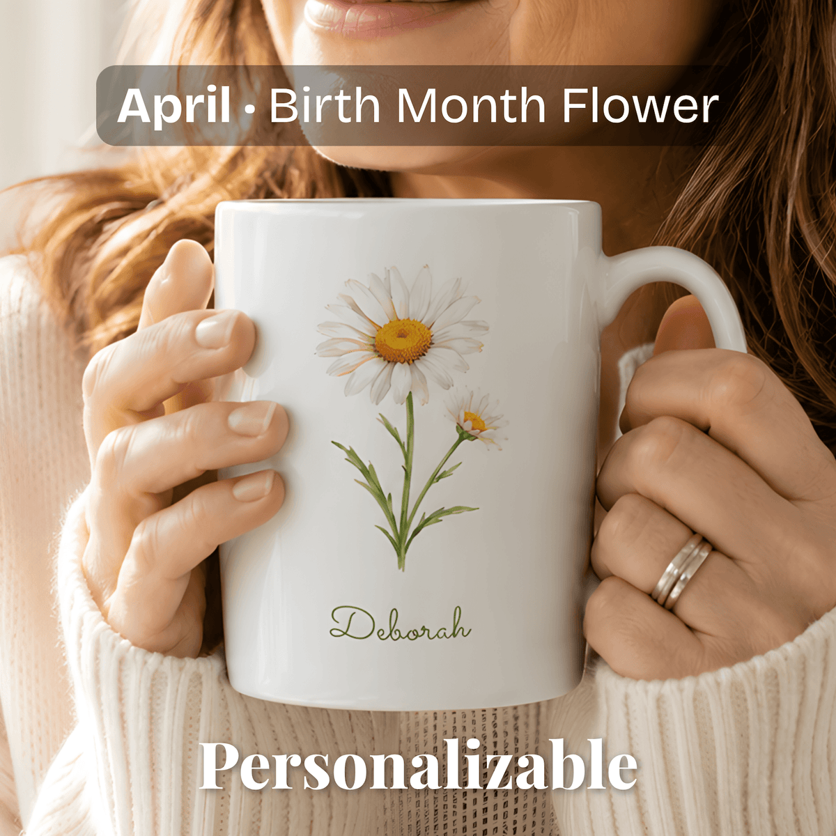 A woman holds a white ceramic mug with daisy birth flower and personalized name at bottom.
