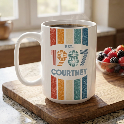 A white ceramic 15oz coffee mug with a retro 1987 design, sitting on a wooden cutting board in a kitchen setting with a bowl of fresh berries in the background.