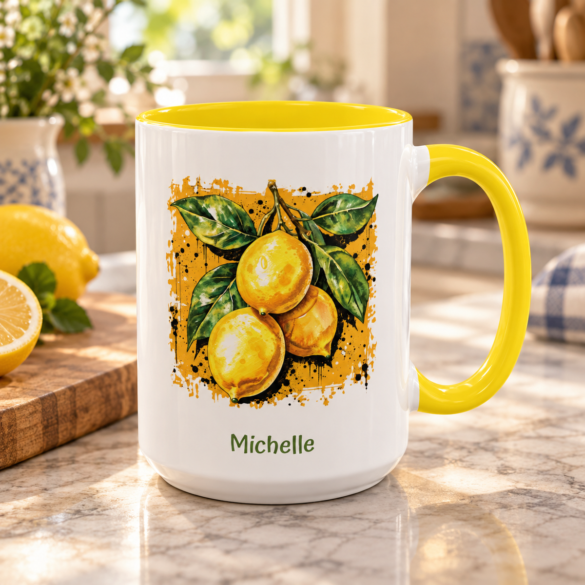 A white ceramic 15oz mug with a bright yellow handle and interior, featuring a printed illustration of three lemons with green leaves on a dark yellow textured background, with the name 'Michelle' printed below. The mug is set on a marble kitchen counter with lemons and a cutting board in the background.