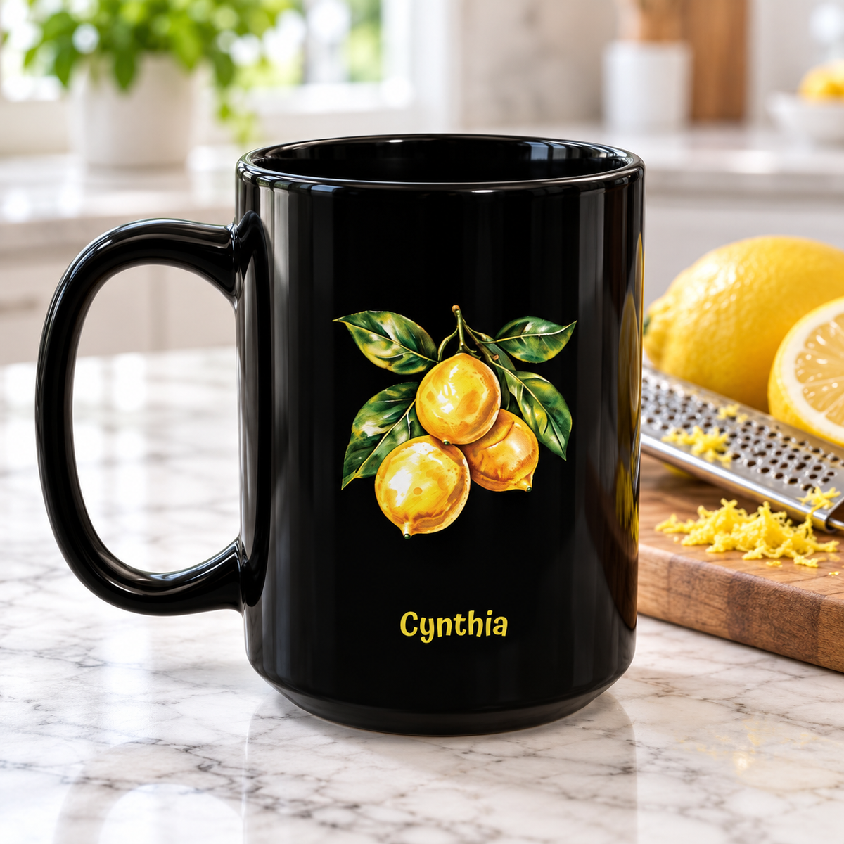 A glossy black 15oz ceramic mug with a printed illustration of three yellow lemons on a branch with green leaves and the name 'Cynthia' in yellow text below. The mug is set on a marble kitchen countertop with lemons, a grater, and a blurred kitchen background.