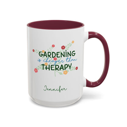 A white ceramic 15oz mug with a maroon colored handle and interior, featuring the printed phrase 'GARDENING is cheaper than THERAPY' in green and blue script with small colorful flowers, and the name 'Jennifer' in green cursive below. Right handle view.