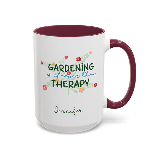 A white ceramic 15oz mug with a maroon colored handle and interior, featuring the printed phrase 'GARDENING is cheaper than THERAPY' in green and blue script with small colorful flowers, and the name 'Jennifer' in green cursive below. Right handle view.