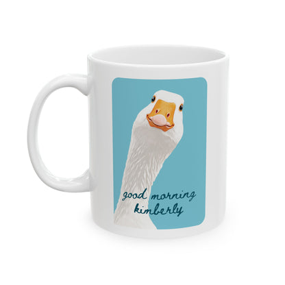 A white ceramic 15oz mug featuring a printed graphic of a white goose head with an orange beak on a light blue background, with the text 'good morning kimberly' written below in dark blue script. Left handle view.
