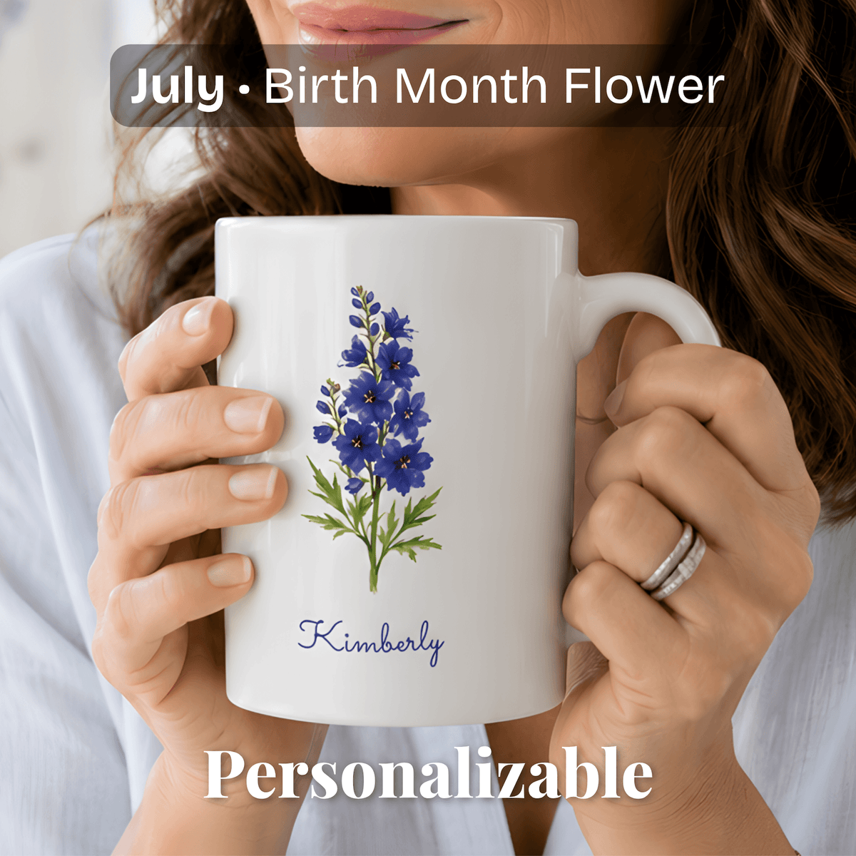 A woman holds a white ceramic mug with larkspur birth flower and personalized name at bottom.