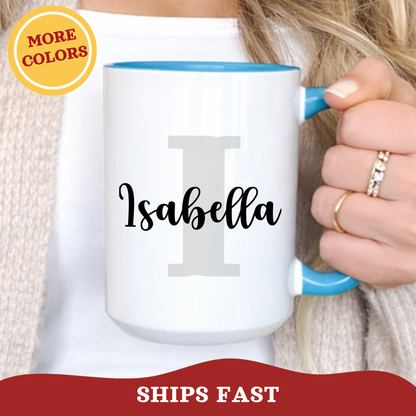 Person holding a personalized layered name and initial ceramic light blue mug with a colorful accent handle, with grey block initial 'I' and name Isabella printed over in a joyful script font.