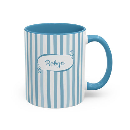 A ceramic 11oz mug with vertical light blue and white stripes, a solid blue handle and interior, and a white label on the front that reads 'Robyn' in blue script. Right handle view.