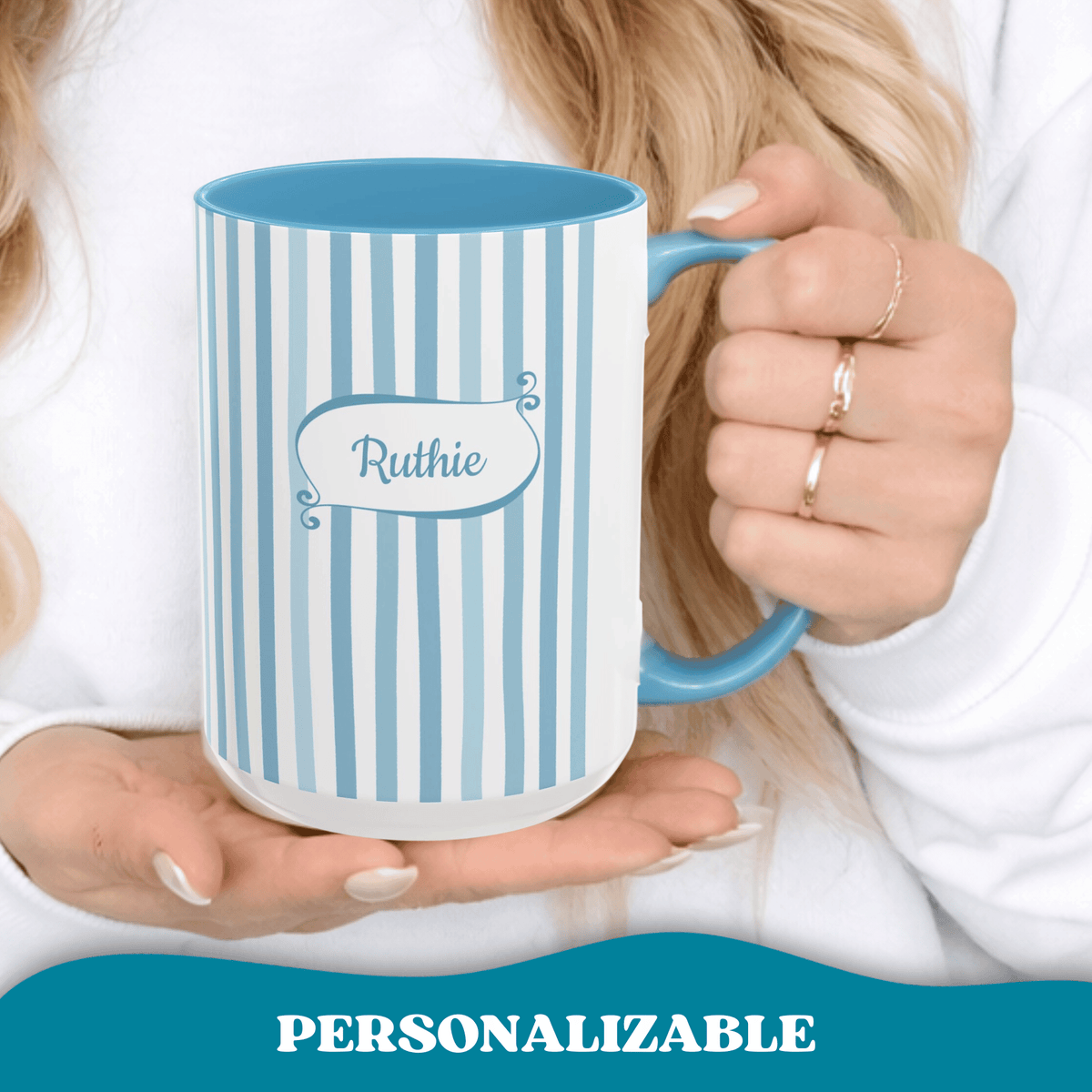 A person in a white top holds a ceramic 15oz mug with light blue and white vertical stripes, a blue handle and interior, and a personalized name in a playful frame reading 'Ruthie'. A banner at the bottom says 'PERSONALIZABLE'.