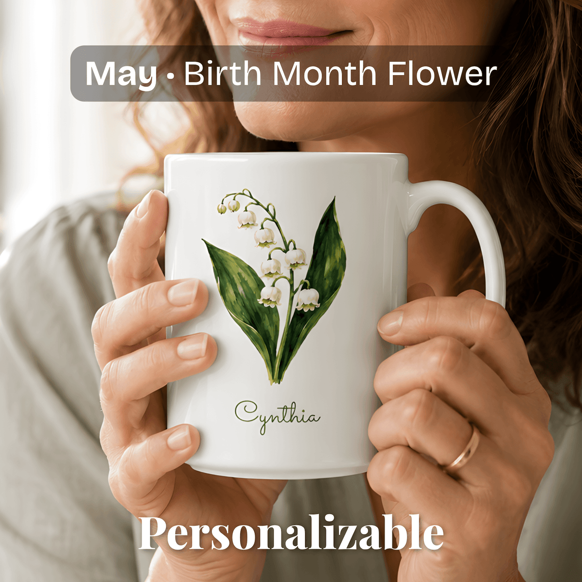 A woman holds a white ceramic mug with lily of the valley birth flower and personalized name at bottom.
