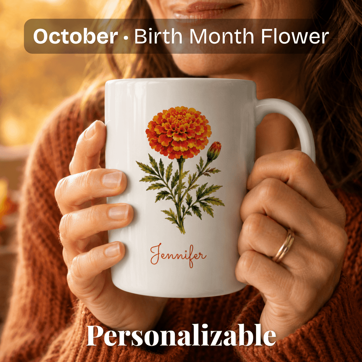 A woman holds a white ceramic mug with marigold birth flower and personalized name at bottom.
