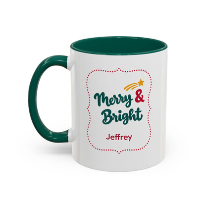 A white ceramic 11oz mug with a dark green handle and interior, featuring a festive graphic in thick script lettering that reads 'Merry & Bright' with a red dotted border, a small yellow shooting star, and the name 'Jeffrey' printed below. Left handle view.