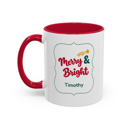A white ceramic 11oz mug with a red interior and red handle, featuring a 'Merry & Bright' holiday graphic in bold red script lettering, and the personalized name 'Anne-Marie' printed on the front, set against a plain white background. Left handle view.