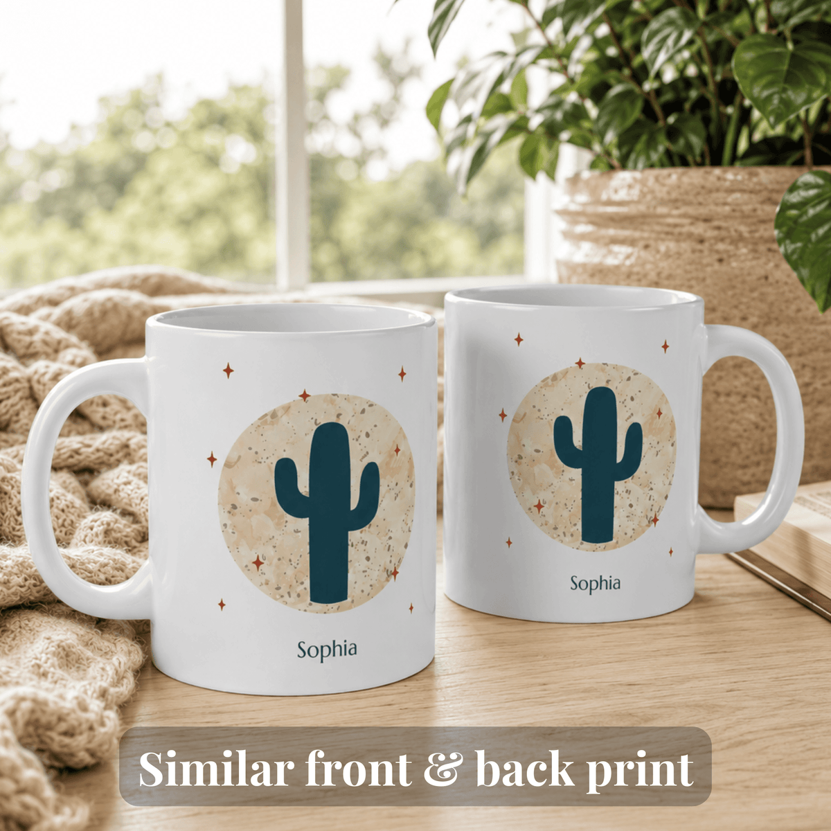 Two white 11oz ceramic mugs displayed on a wooden table in a cozy indoor setting, showing the front and back designs. The mugs feature a dark teal cactus inside a textured beige circle with small orange stars, and the name Jocelyn printed below.
