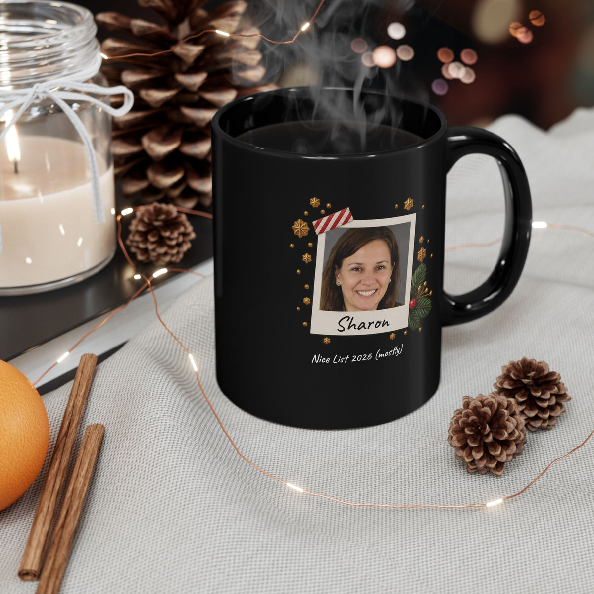 A black ceramic 11oz mug with a custom printed holiday design featuring a photo frame, gold ornaments, and the name 'Abigail' with the text 'Nice List 2026 (mostly)' placed on table cloths with pinecones, cinnamon and a candle. Right handle view.