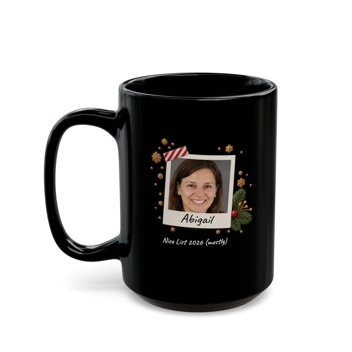 A black ceramic 15oz mug with a custom printed holiday design featuring a photo frame, gold ornaments, and the name 'Abigail' with the text 'Nice List 2026 (mostly)' on a white background. Left handle view.