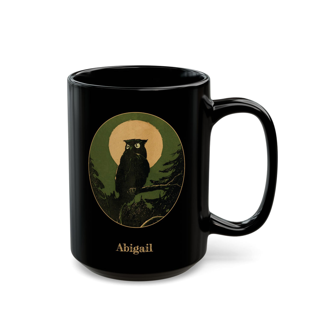 A black ceramic mug with a handle, featuring a circular graphic of an owl perched on a branch in front of a gold color moon, with the name 'Abigail' printed below in a gold-like color.