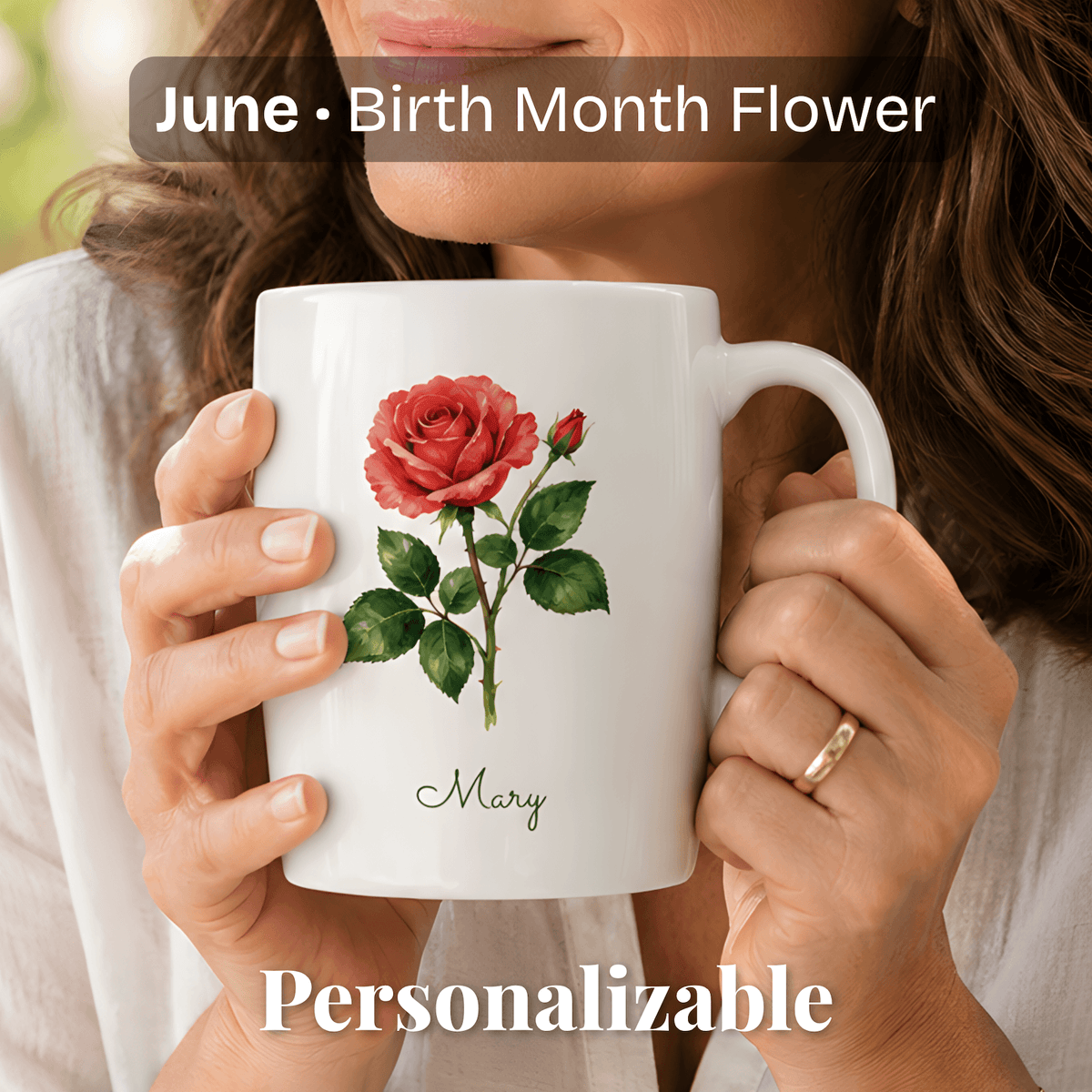 A woman holds a white ceramic mug with rose birth flower and personalized name at bottom.