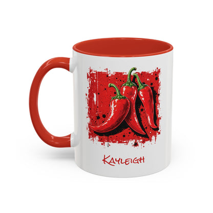 A white ceramic 11oz mug with a red handle and red interior, featuring a graphic of three red chili peppers on a red splattered square and the name 'KAYLEIGH' printed below in red script. Left handle view.