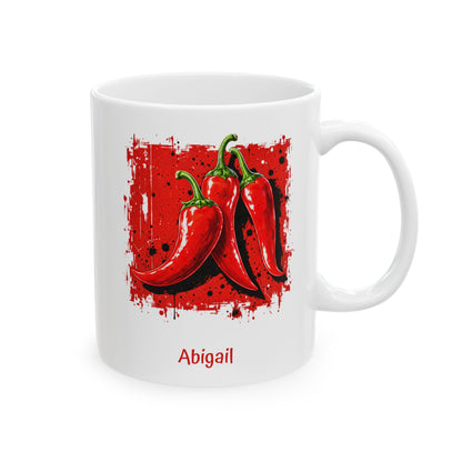 A white ceramic 11oz mug featuring a graphic print of three red chili peppers on a red splattered background, with the name 'Abigail' printed in red below the illustration. Right handle view.