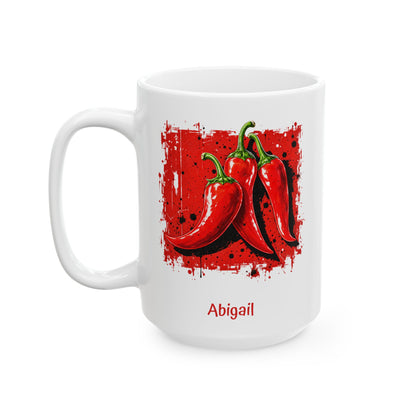 A white ceramic 15oz mug featuring a graphic print of three red chili peppers on a red splattered background, with the name 'Abigail' printed in red below. Left handle view.