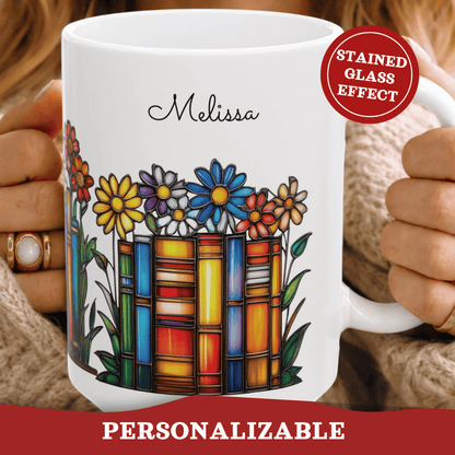 A white ceramic mug with a stained-glass-style book and flower design, held by two hands wearing a beige knit sweater. The mug is personalized with the name 'Melissa' in black script.