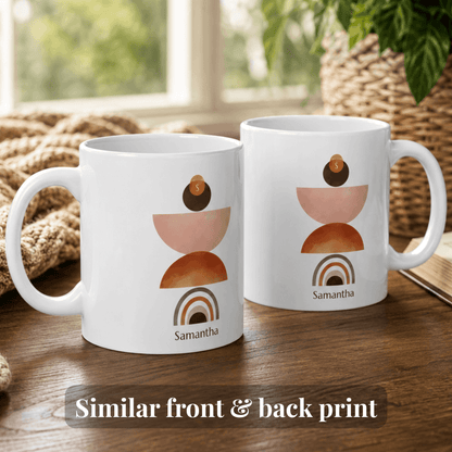 Two white ceramic 11oz mugs with a stacked geometric art print in terracotta, peach, and brown, featuring the name 'Samantha' and a small coin detail, displayed on a wooden table with a cozy background.