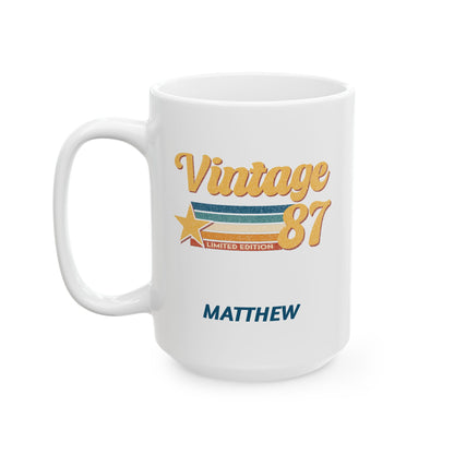 A white ceramic 15oz mug with a 'Vintage 87' graphic in gold, orange, and blue, featuring the name 'MATTHEW' printed below in blue, shown on a clean white background. Left handle view.