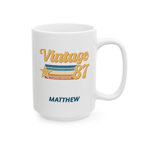 A white ceramic 15oz mug with a 'Vintage 87' graphic in gold, blue, and orange, featuring the name 'MATTHEW' printed below in blue, shown on a clean white background. Right handle view.