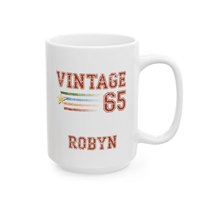 A white ceramic 15oz mug with a custom printed design featuring the text 'VINTAGE 65 ROBYN' in a distressed red font, with a small horizontal multicolor stripe and star graphic in the center, on a white background. Right handle view.