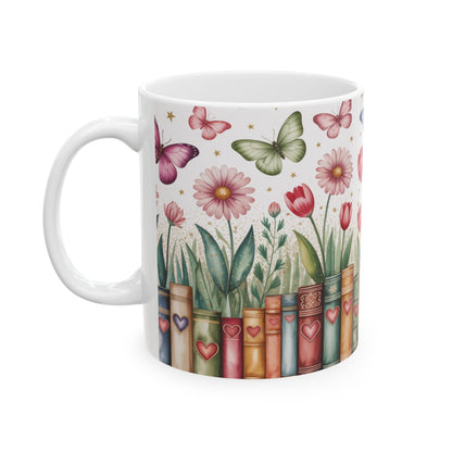 A white ceramic 11oz mug decorated with a whimsical illustration of book spines, flowers, butterflies, and leaves on a white background. Left handle view.