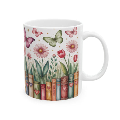 A white ceramic 11oz mug featuring a printed design of vintage book spines decorated with hearts, with flowers and butterflies growing out of them, on a white background. A subtle personalizable name on one of the book spines. Right handle view.