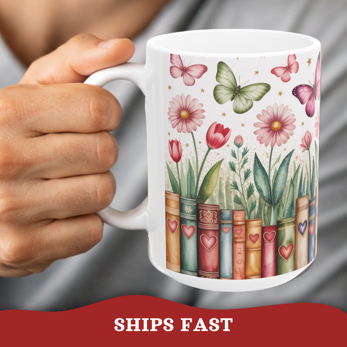 A white ceramic 15oz mug held by a male person, featuring a printed design of vintage book spines decorated with hearts, with flowers and butterflies growing out of them, on a white background.