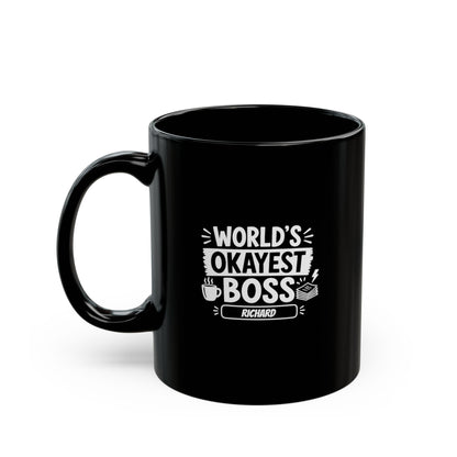 Black 11oz mug with white illustrative typographic design saying 'World's Okayest Boss' and a personalized name at the bottom, left handle view. Mug is placed on a white background.