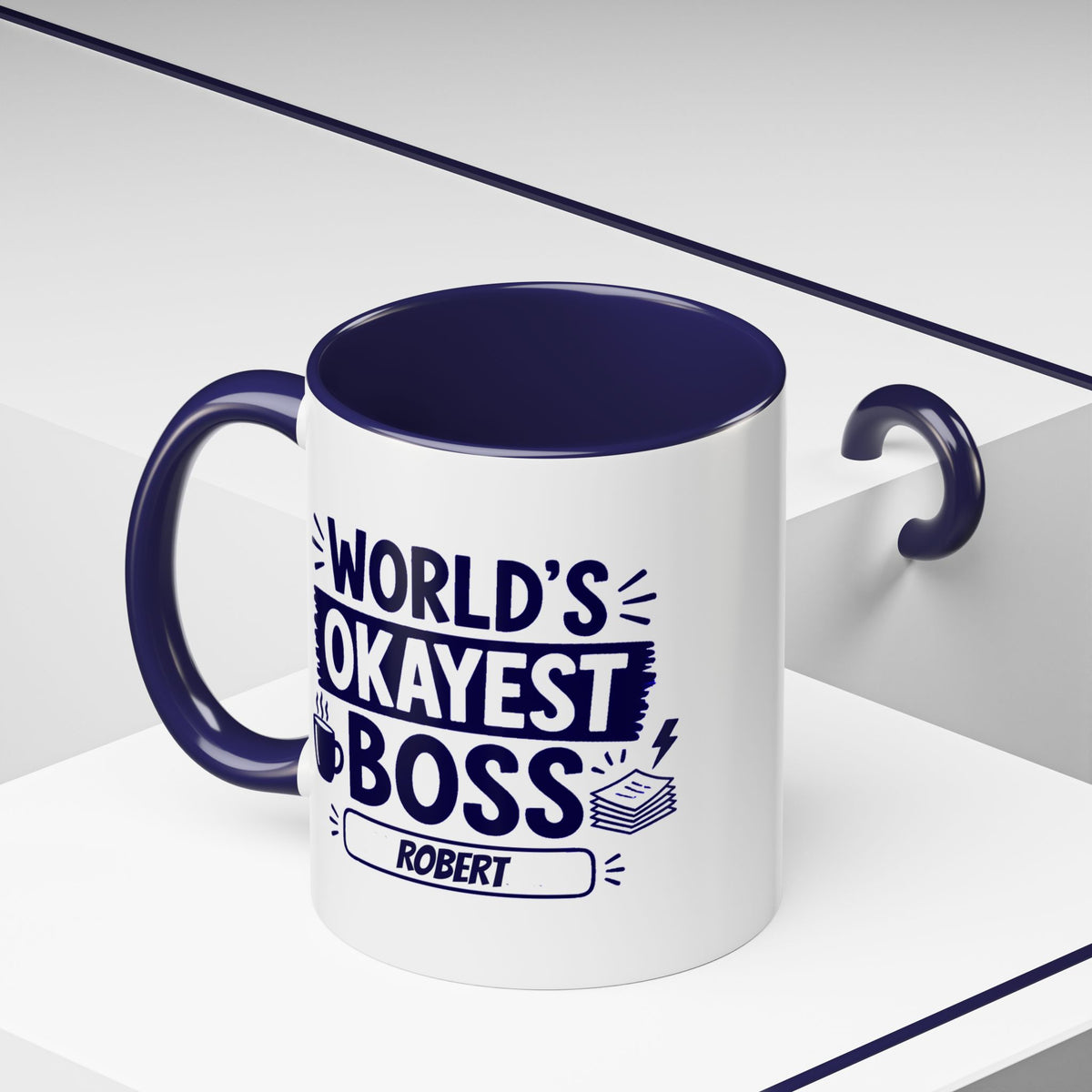 A white ceramic 11oz mug with a dark navy blue handle, interior, and printed text reading 'WORLD'S OKAYEST BOSS' and 'ROBERT' in navy blue lettering, shown on a clean white geometric background.